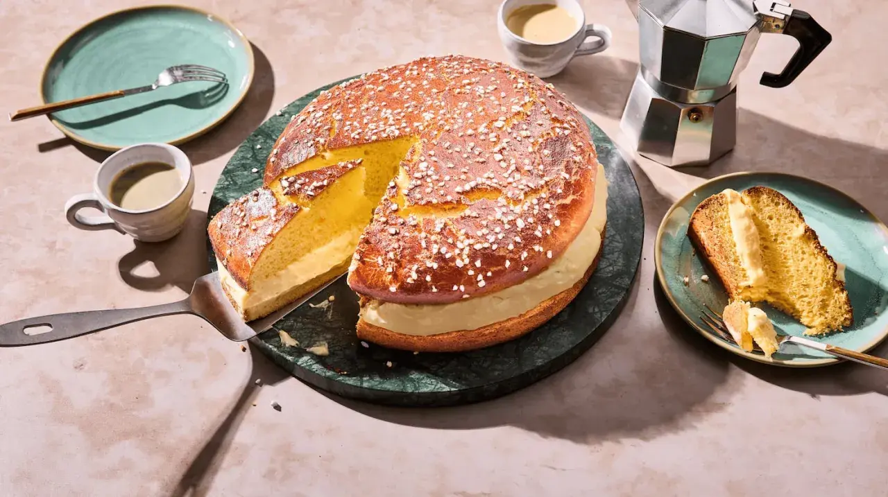 Eine köstliche Tarte Tropezienne, aufgeschnitten und mit einer Kaffeetasse und einem Moka-Topf serviert.