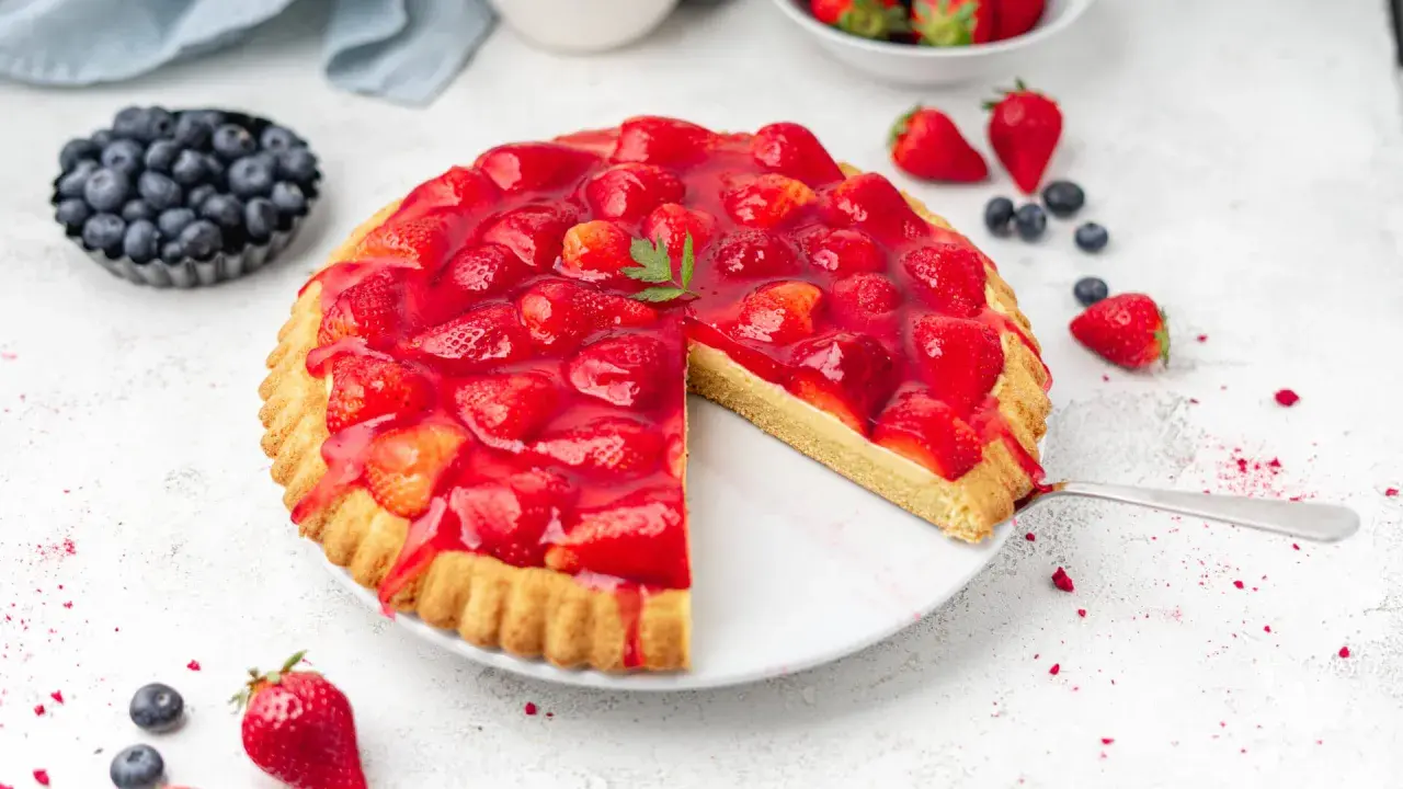 Ein köstlicher obstboden mit erdbeeren, bedeckt mit glänzendem Gelee. Daneben Blaubeeren und frische Erdbeeren.