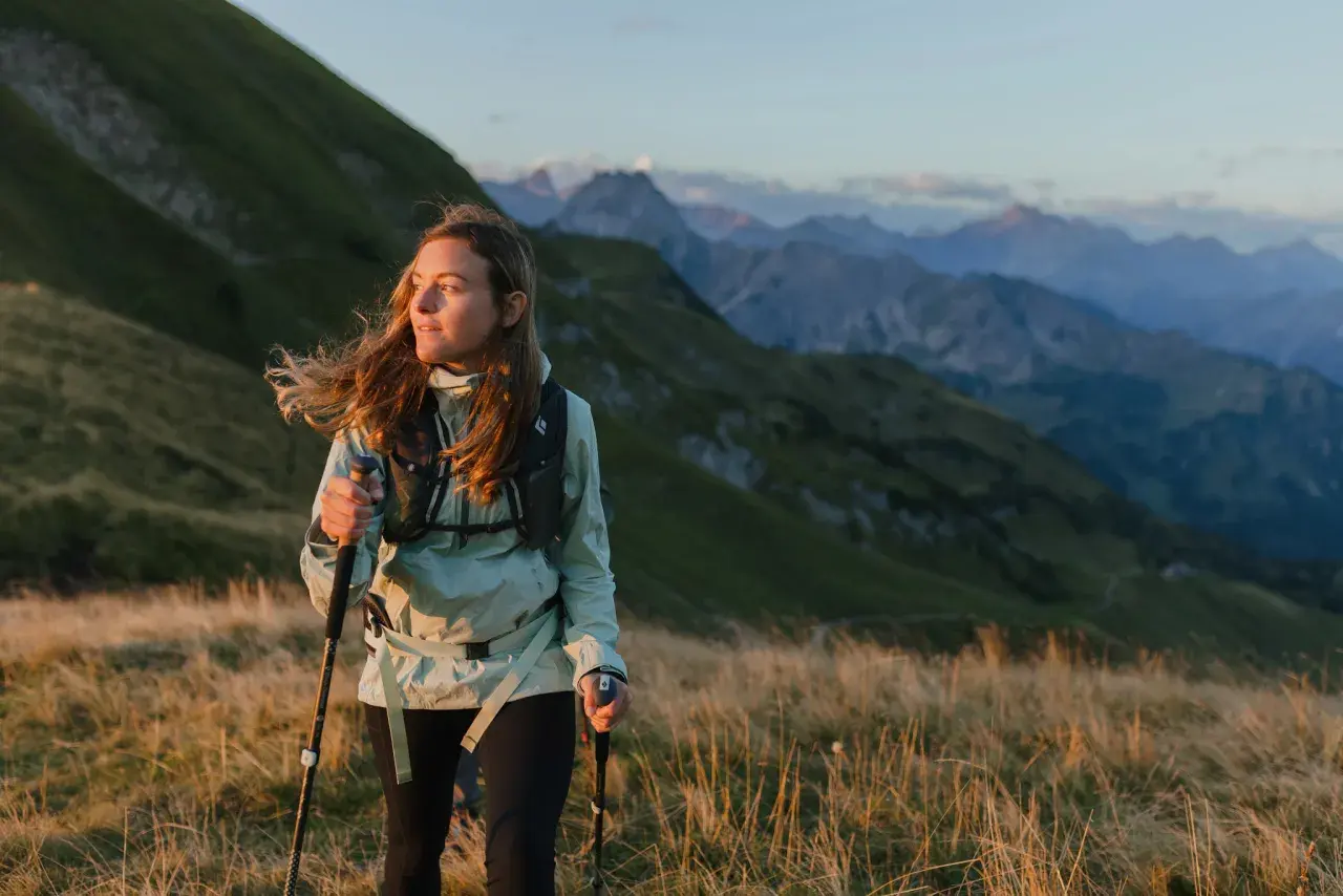 Kobieta z kijkami do **speed hikingu** podziwia alpejski krajobraz o zachodzie słońca.