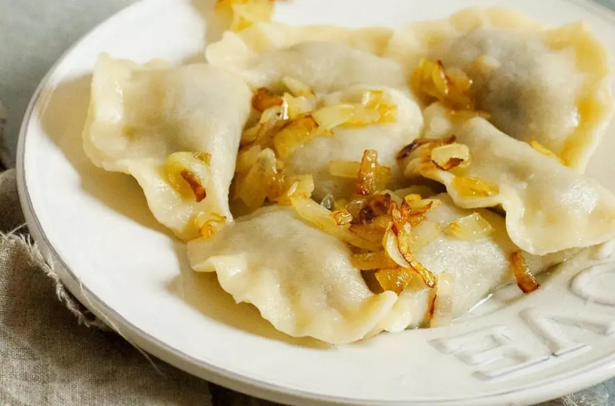 Pyszne pierogi ruskie na talerzu, polane skwarkami z cebulki. Idealne, gdy wiesz, jak długo gotować pierogi ruskie.