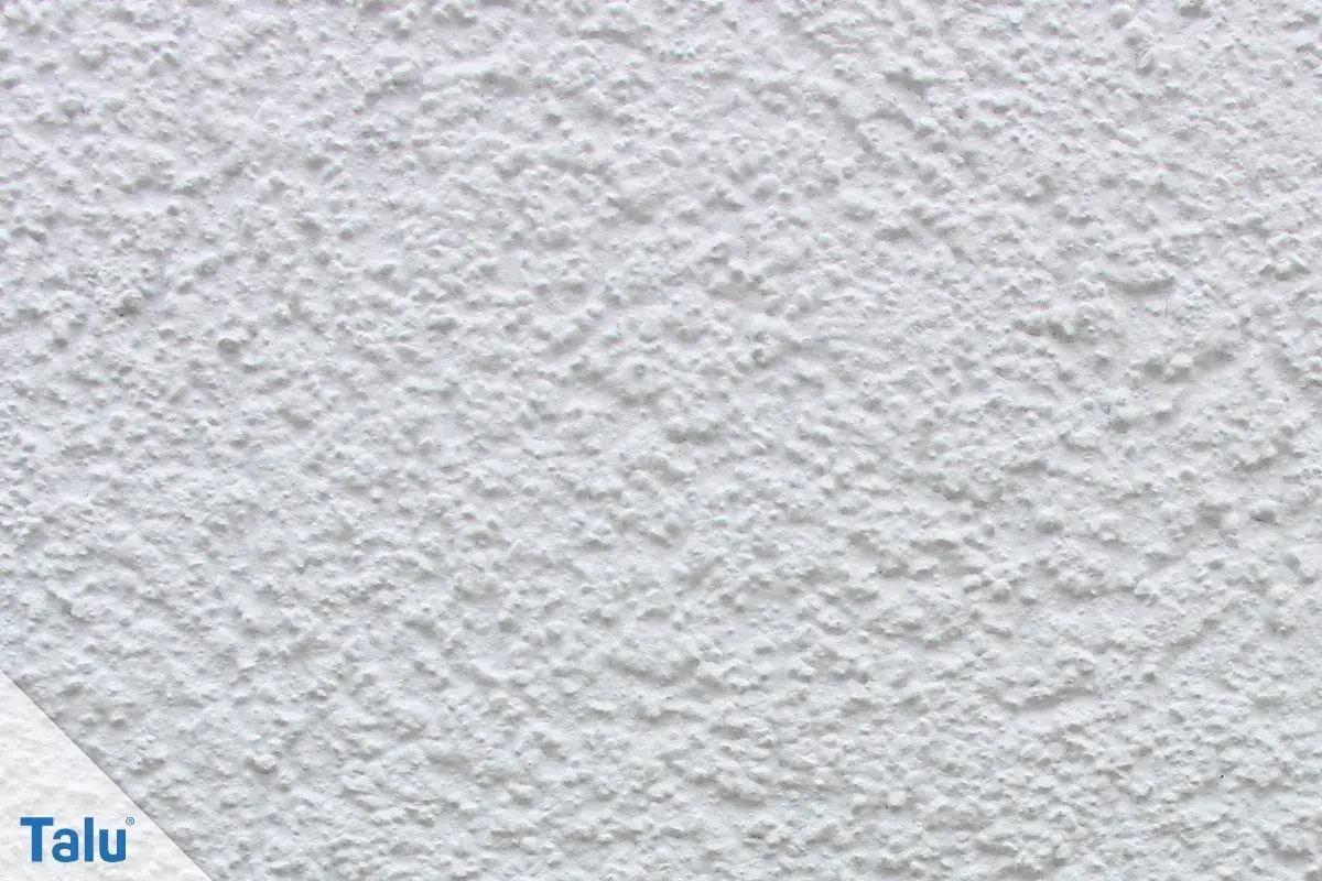 Nahaufnahme einer weißen, strukturierten Wand, die zeigt, wie man eine Wand verputzt. Das Korn ist unregelmäßig und erzeugt eine interessante Textur.