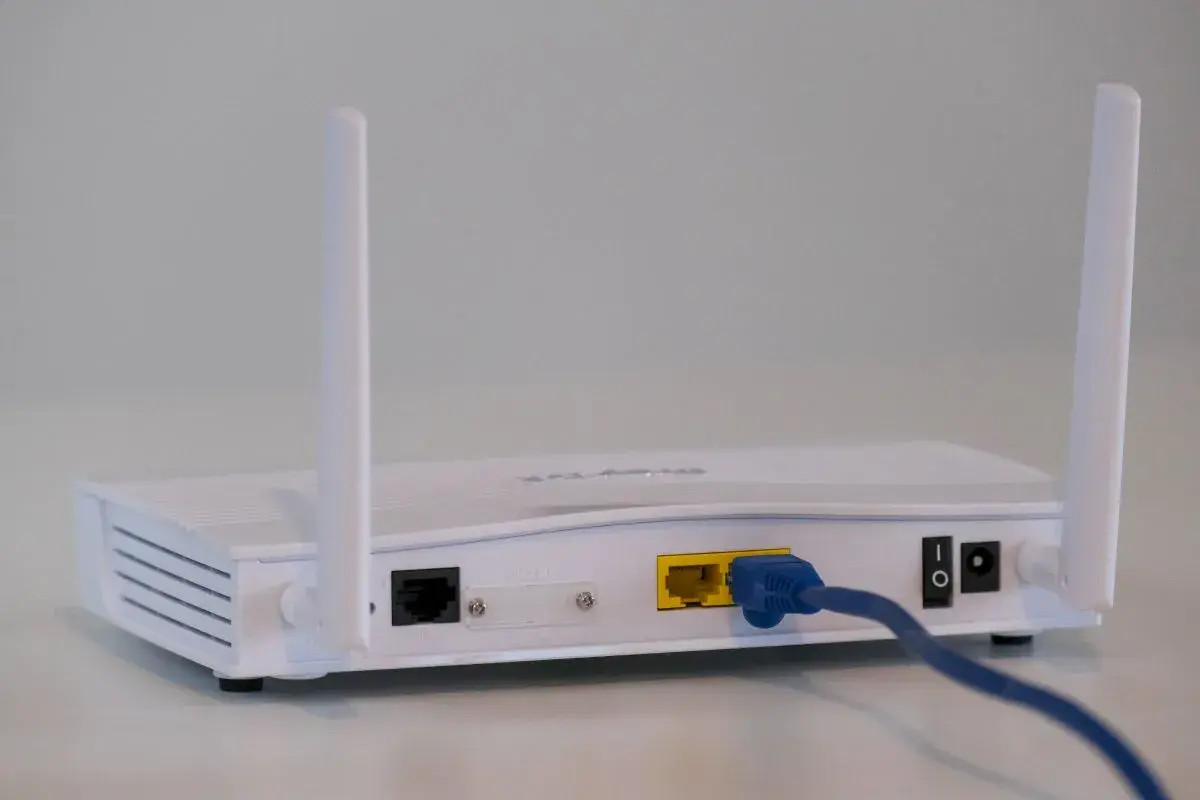 Biały router z dwiema antenkami. Widoczne porty LAN, zasilania i przycisk włączania. To urządzenie, czym się różni modem od routera, rozdziela internet.