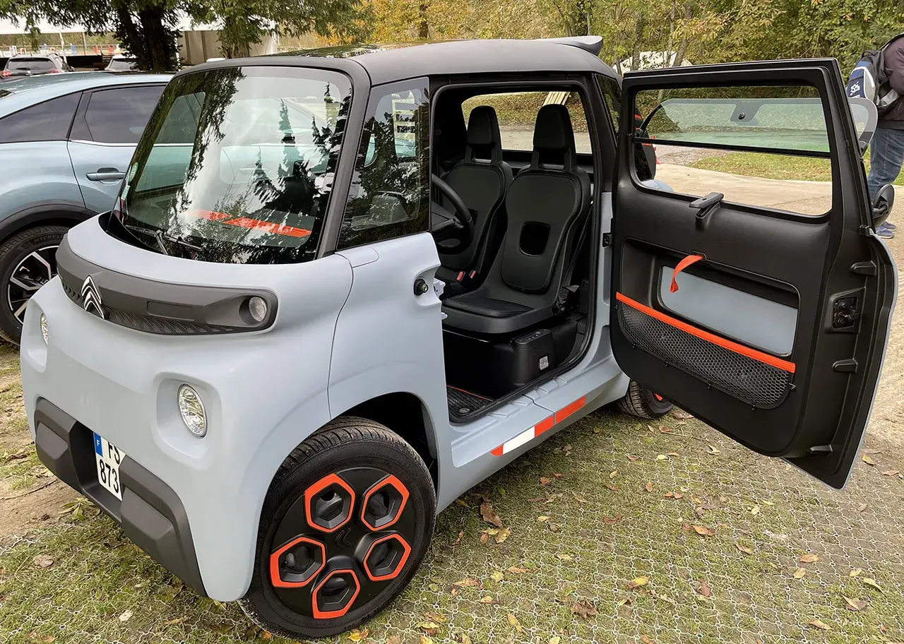 Citroën Ami, un quadriciclo elettrico compatto, con porte aperte e interni visibili. Il suo design unico e le dimensioni ridotte lo rendono perfetto per la città.