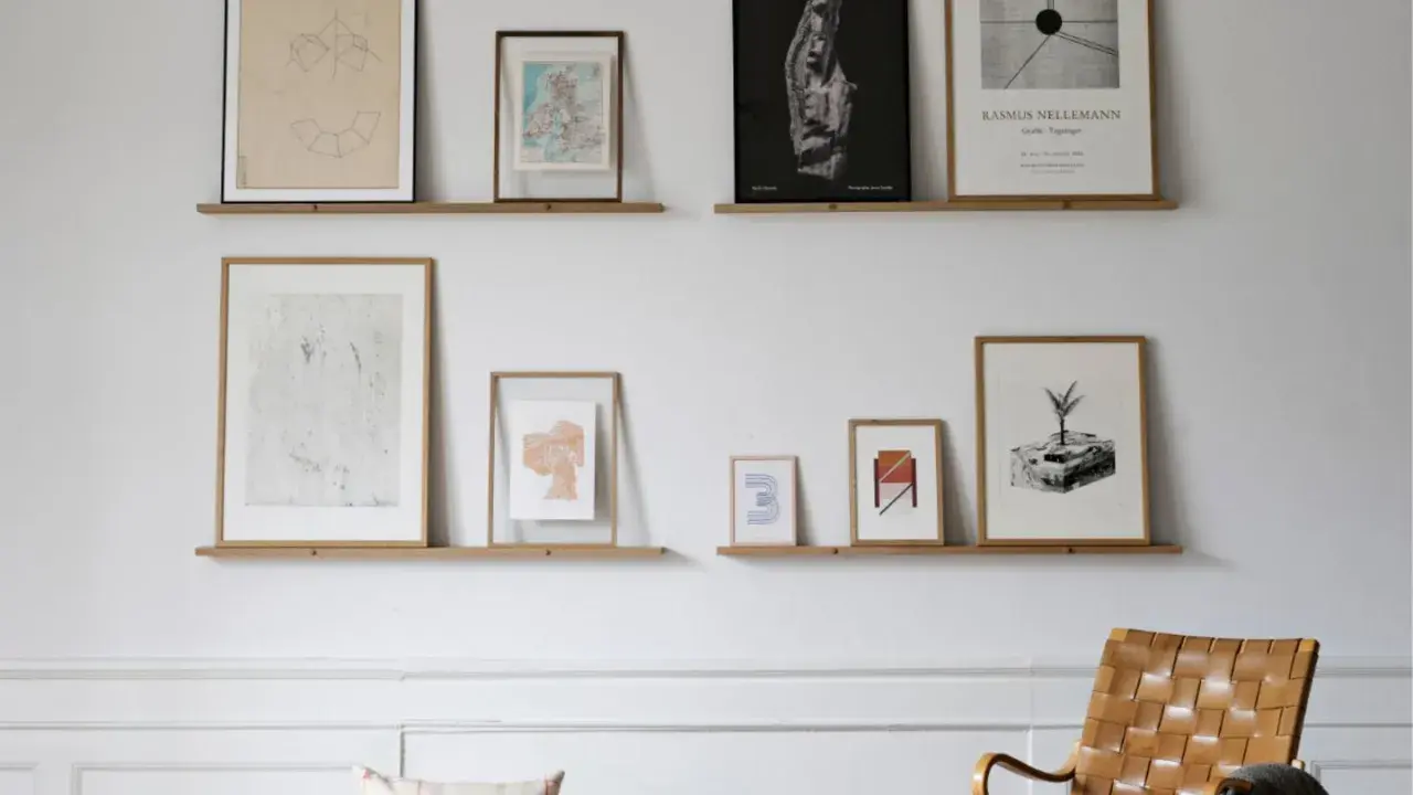 Bilderleiste dekorieren wohnzimmer: Mehrere gerahmte Kunstwerke und Karten zieren zwei schlichte Holzregale, die eine stilvolle Wandgestaltung im Wohnzimmer bilden.