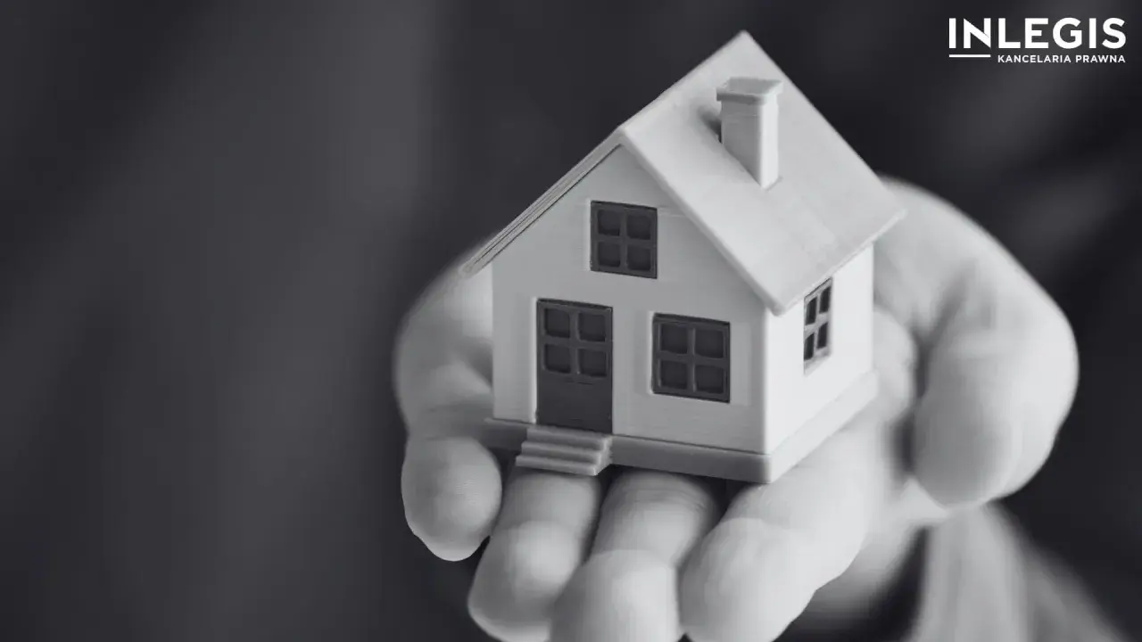 Miniatura domu na dłoni, symbolizująca ograniczone prawa rzeczowe i bezpieczeństwo posiadania.
