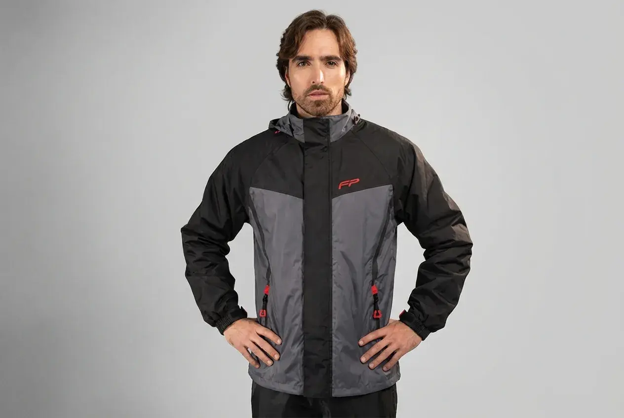 Hombre posando con una prenda impermeable que protege de la lluvia, chaqueta de dos tonos gris y negro con detalles rojos.