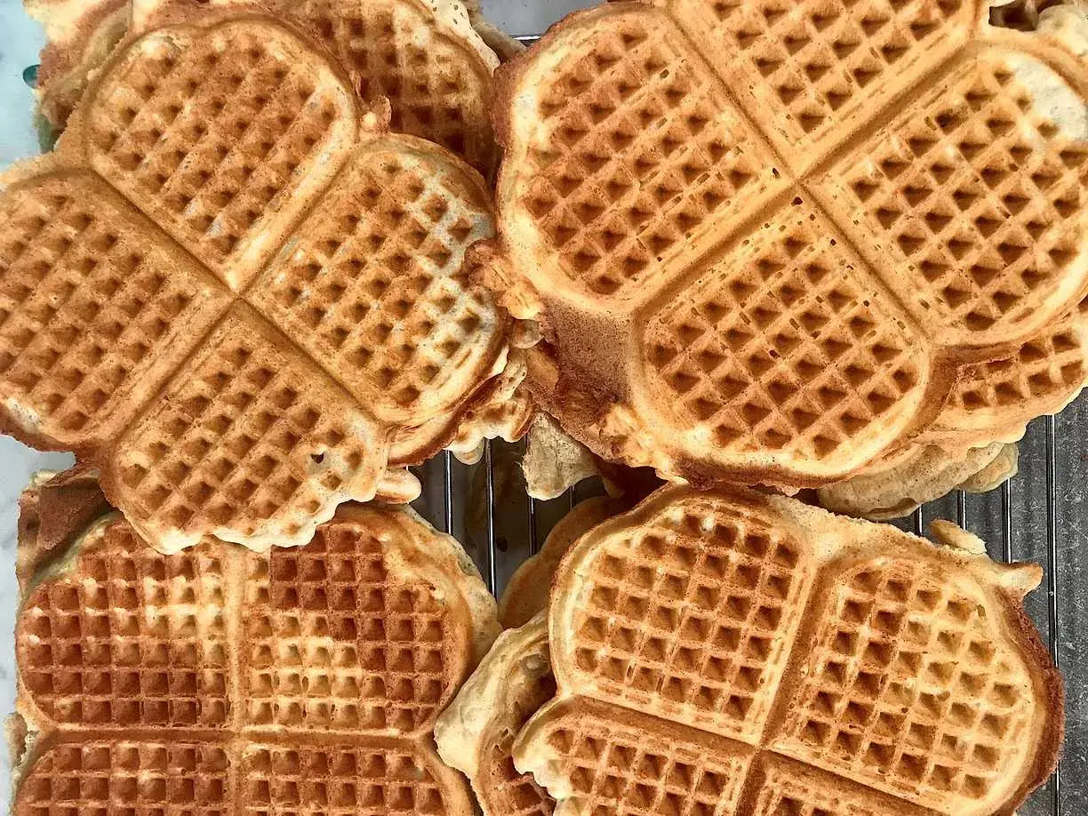 Nygräddade, gyllene glutenfria våfflor ligger staplade på ett galler. Perfekta för en fika!