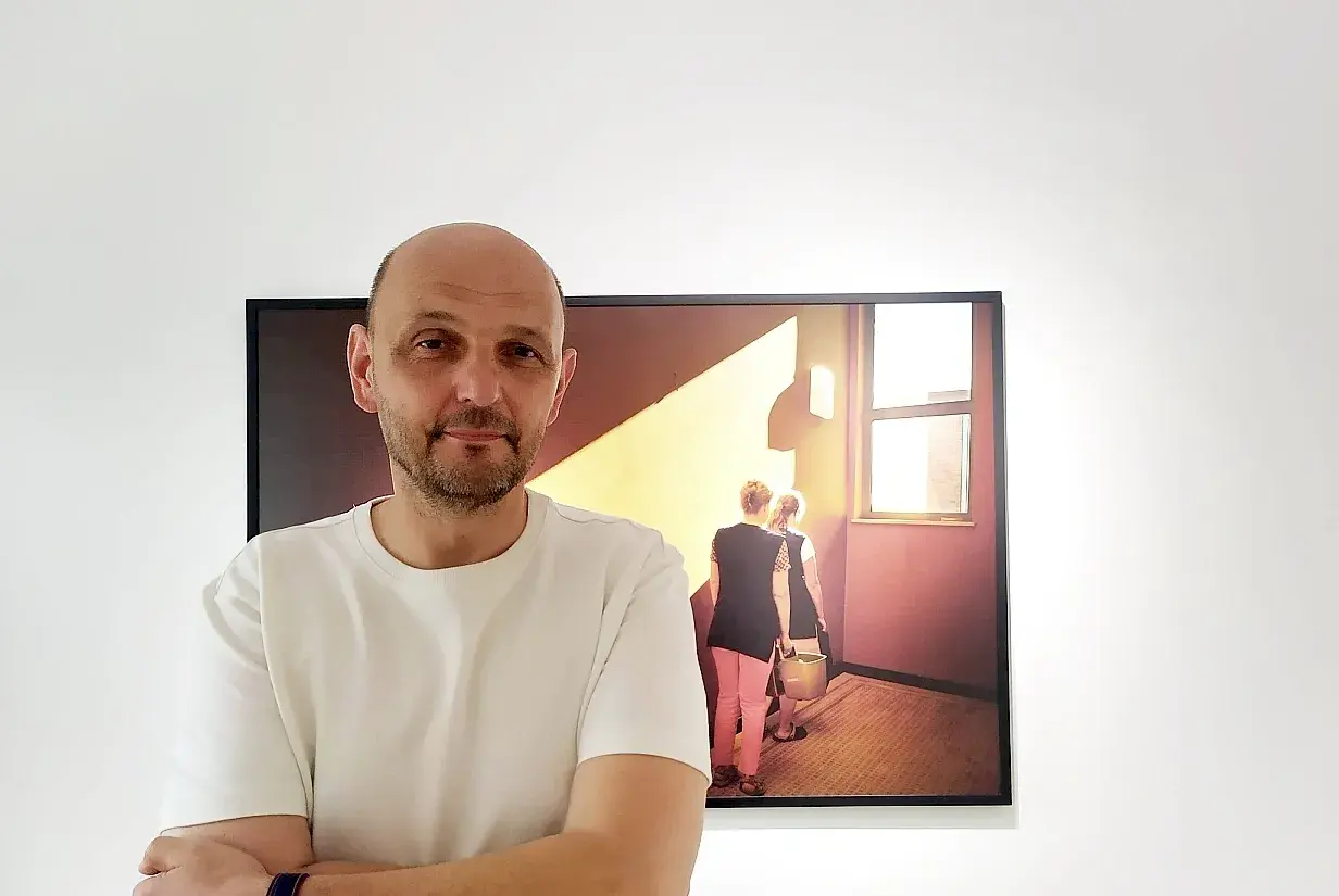 Krzysztof Gołuch obok swojego obrazu z kobietami niosącymi wiadra w świetle.