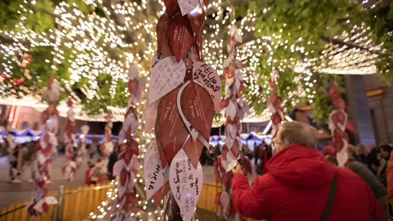 Árbol de deseos en el mercadillo de Navidad de Zaragoza, cubierto de hojas con mensajes y luces festivas.