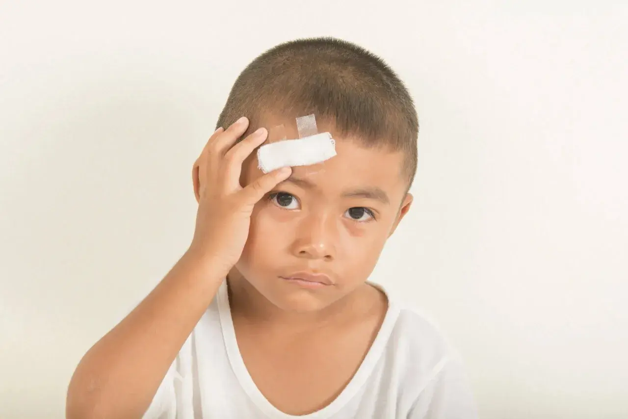 Bambino con cerotto sulla fronte, forse a seguito di un trauma cranico.