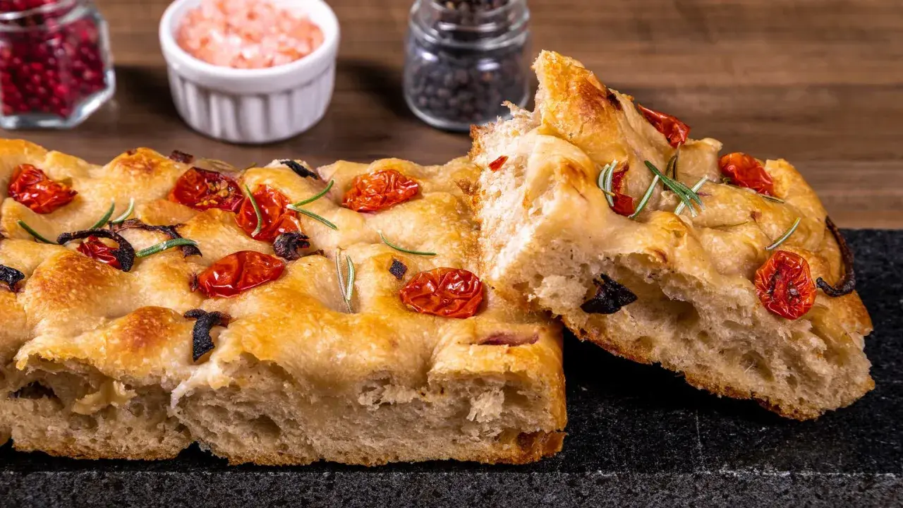 Złocista focaccia z pomidorkami koktajlowymi i rozmarynem, z widocznym puszystym wnętrzem.