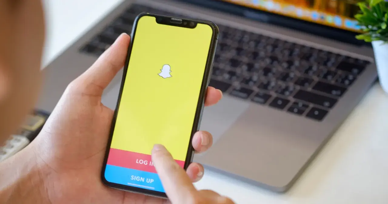 Dłoń trzyma smartfon z logo Snapchata. Widoczny ekran logowania, który może pomóc w procesie jak usunąć konto na snapie.