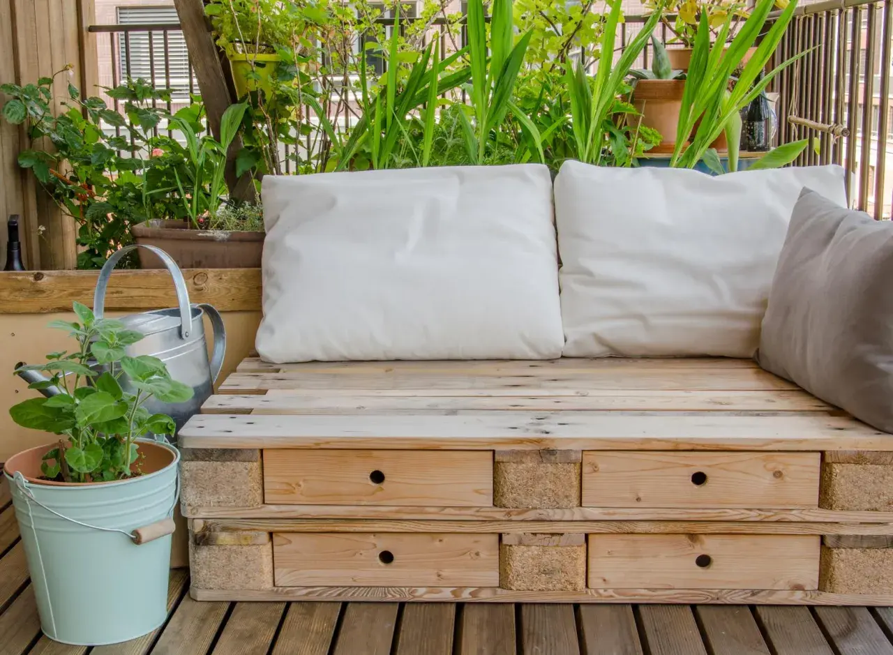 Bequeme Sitzbank aus Paletten mit Schubladen, umgeben von grünen Pflanzen. Tolle Ideen aus Paletten für Balkon und Garten.