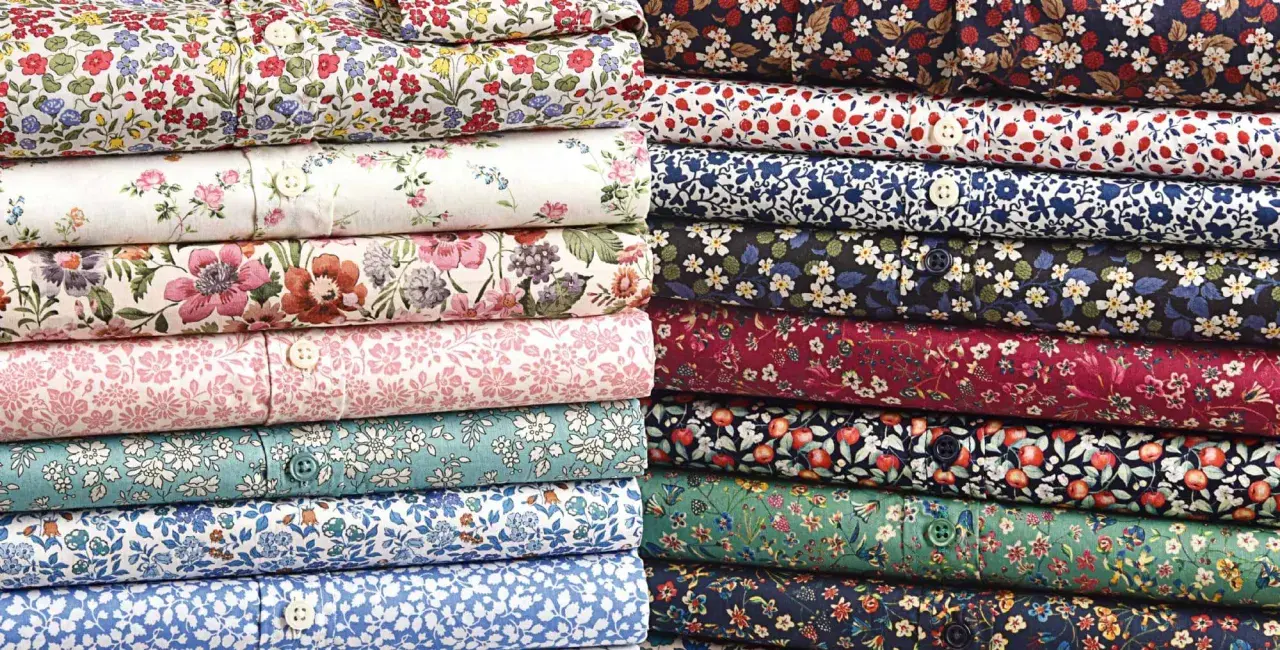 Stacks of folded shirts showcase vibrant, small floral prints, a hallmark of what is liberty fabric.