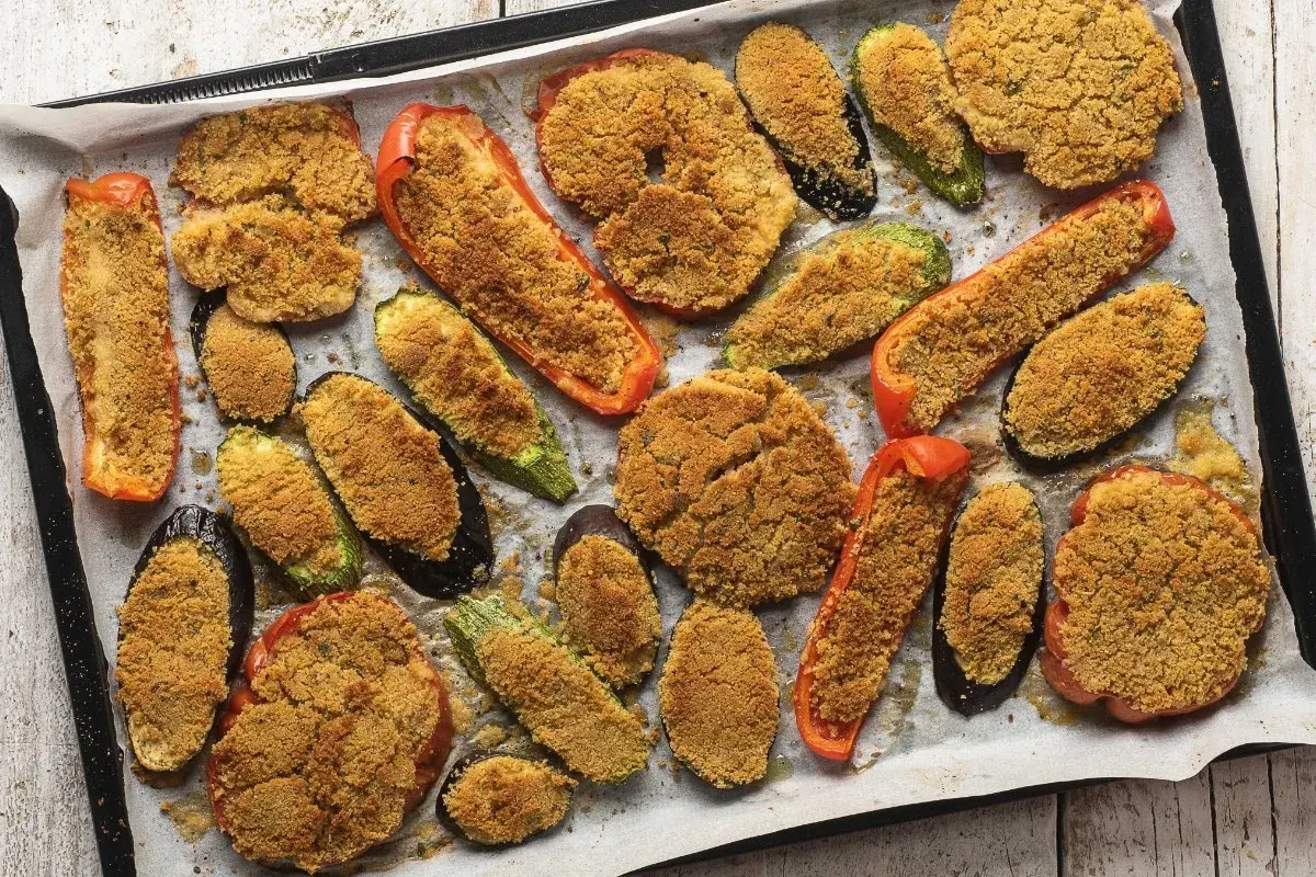 Verdure gratinate al forno con formaggio, un tripudio di sapori e colori su una teglia. Melanzane, zucchine e peperoni ripieni di pangrattato croccante.