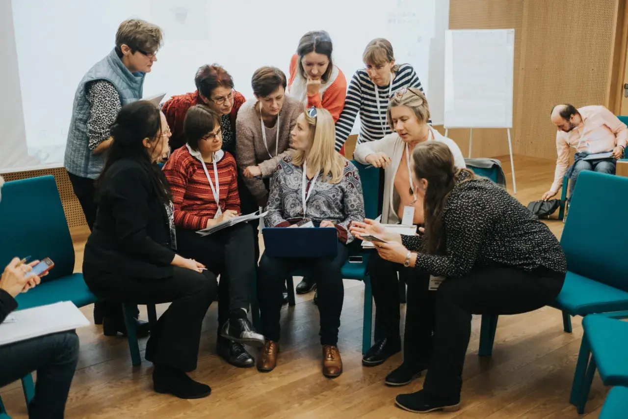 Lehrerinnen und Lehrer im Austausch während einer Hospitation in der Schule. Sie diskutieren und arbeiten an einem Laptop.