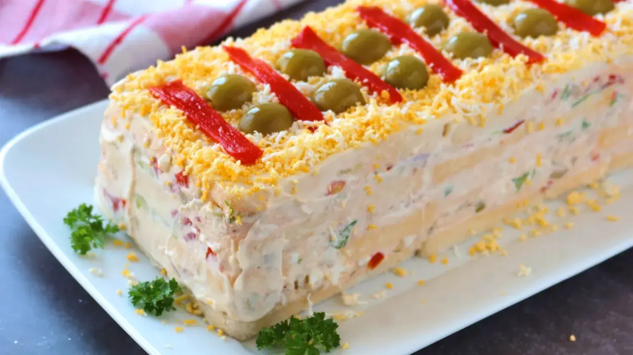 Pastel de atún con pan de molde, decorado con pimientos rojos, aceitunas y huevo rallado. ¡Una delicia!