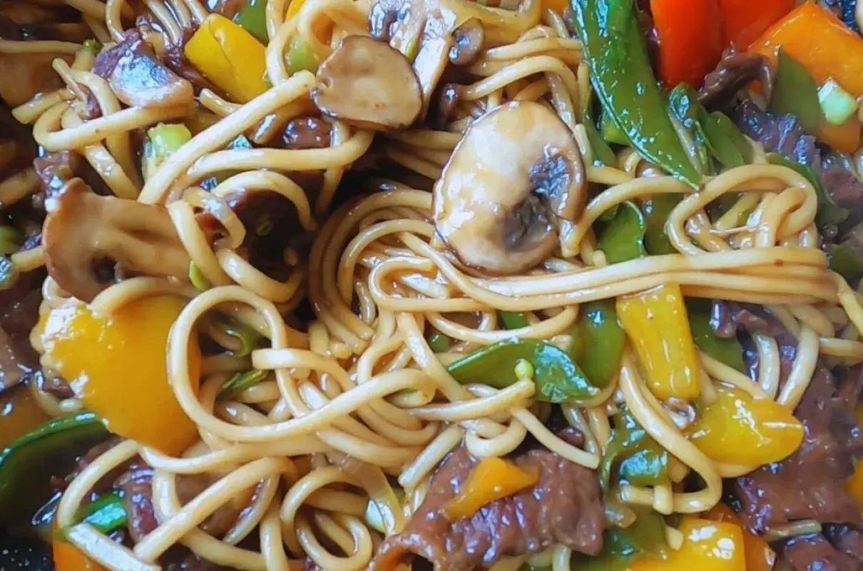 Pyszny makaron chow mein z wołowiną, pieczarkami, papryką i groszkiem cukrowym w sosie.