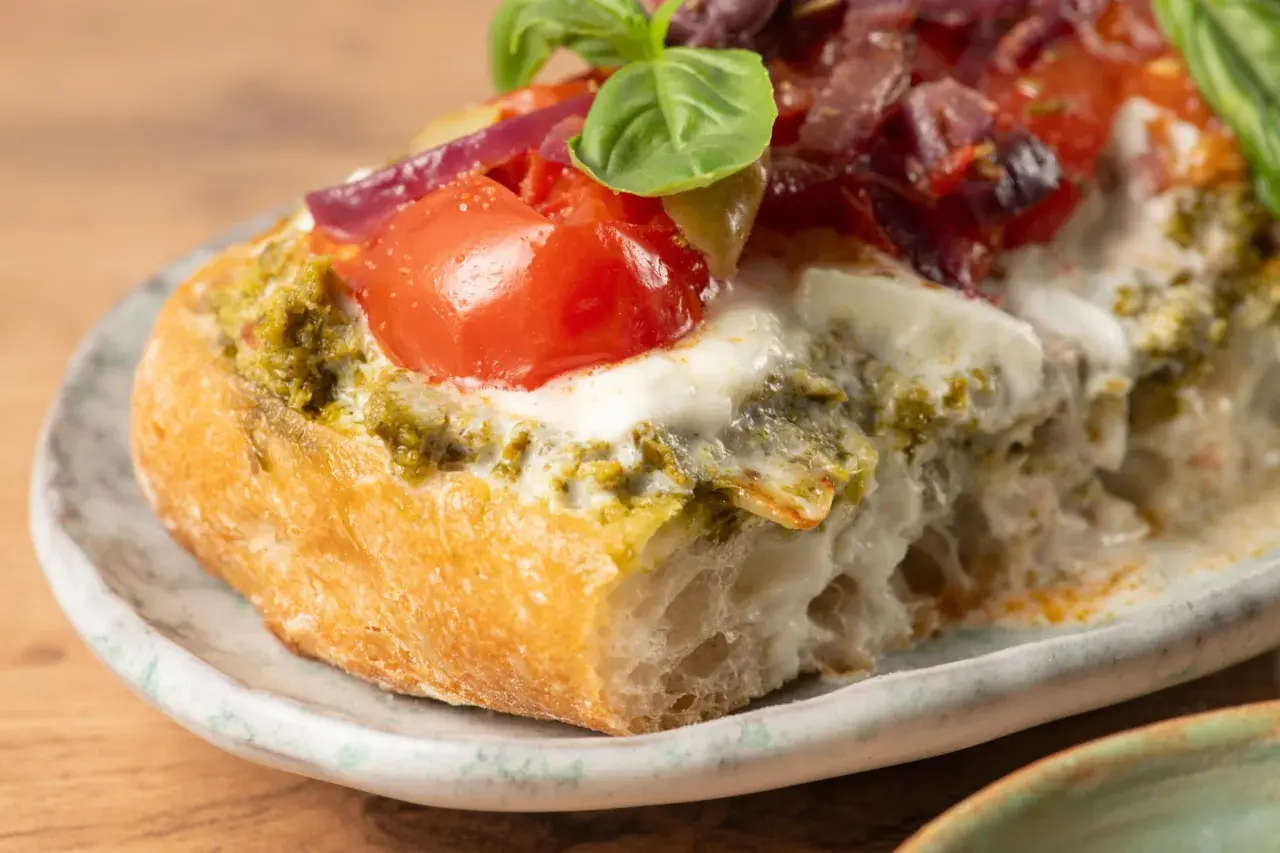 Bruschetta au pesto, tomates fraîches, mozzarella fondante et oignons rouges sur une tranche de pain grillé. Un délice !