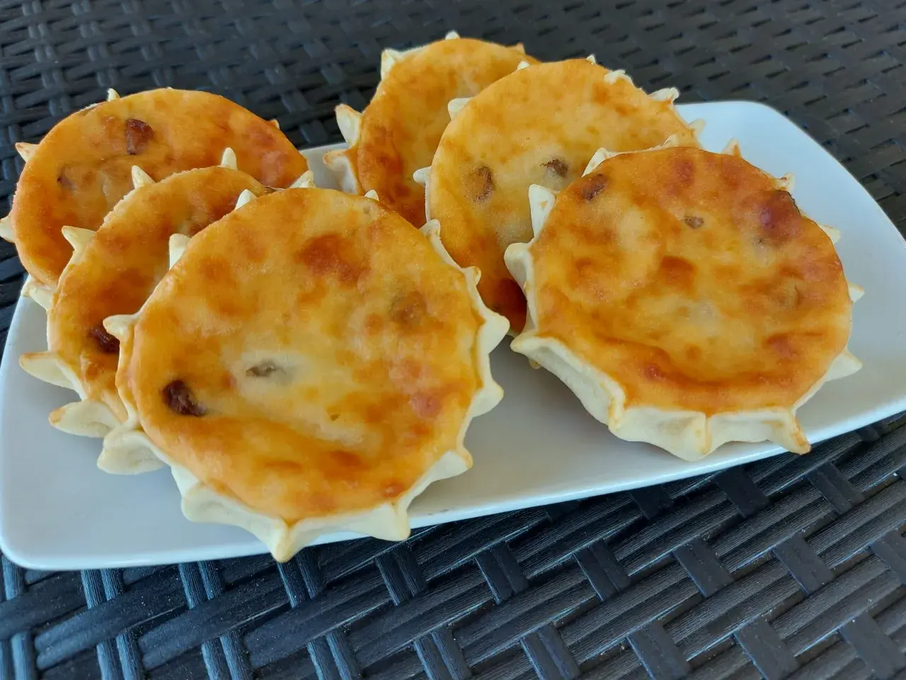 Sei formaggelle di formaggio dorate e invitanti, disposte su un piatto bianco.