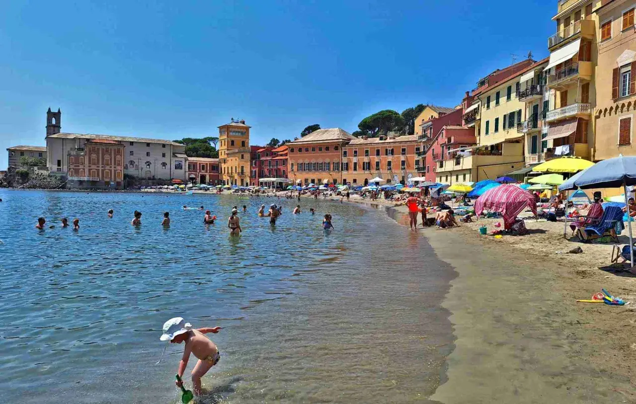 Plage animée à Chiavari, Italie, avec des baigneurs dans l'eau et des parasols colorés sur le sable.