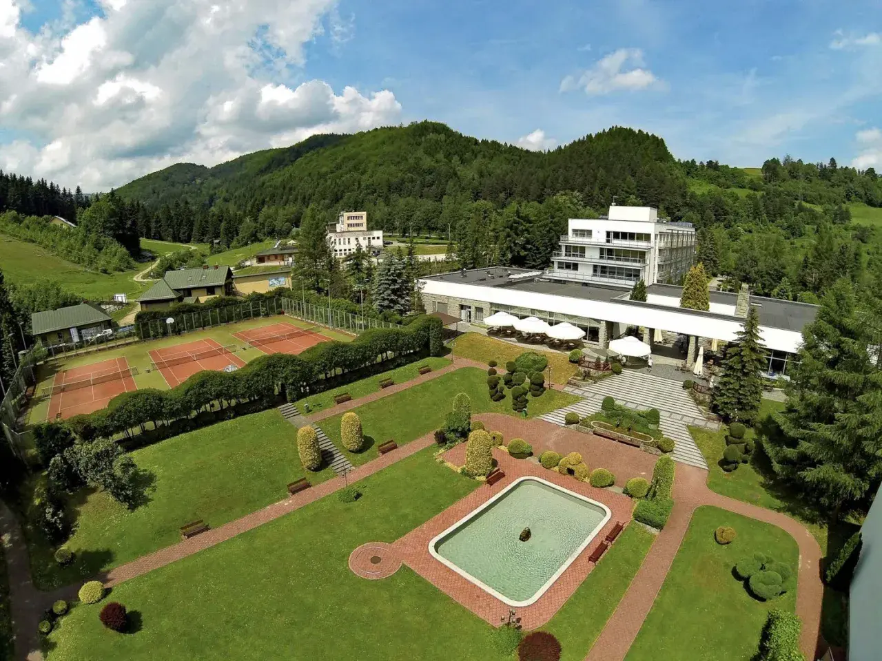 Widok z lotu ptaka na hotel i korty tenisowe w otoczeniu zielonych wzgórz. To Rytro, perła południa, z basenem i zadbanym ogrodem.