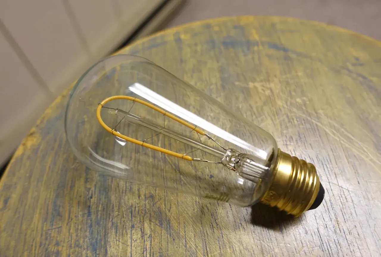 Bombilla de filamento regulable, con un diseño vintage y un filamento amarillo en forma de bucle, descansa sobre una superficie de madera desgastada.