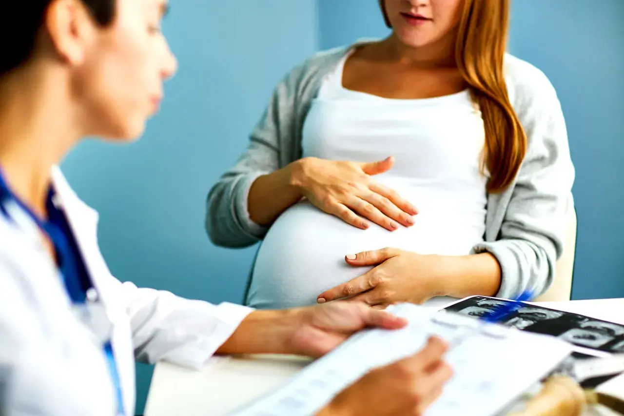 Medico spiega a donna incinta quando si fa la villocentesi, con ecografie sul tavolo.