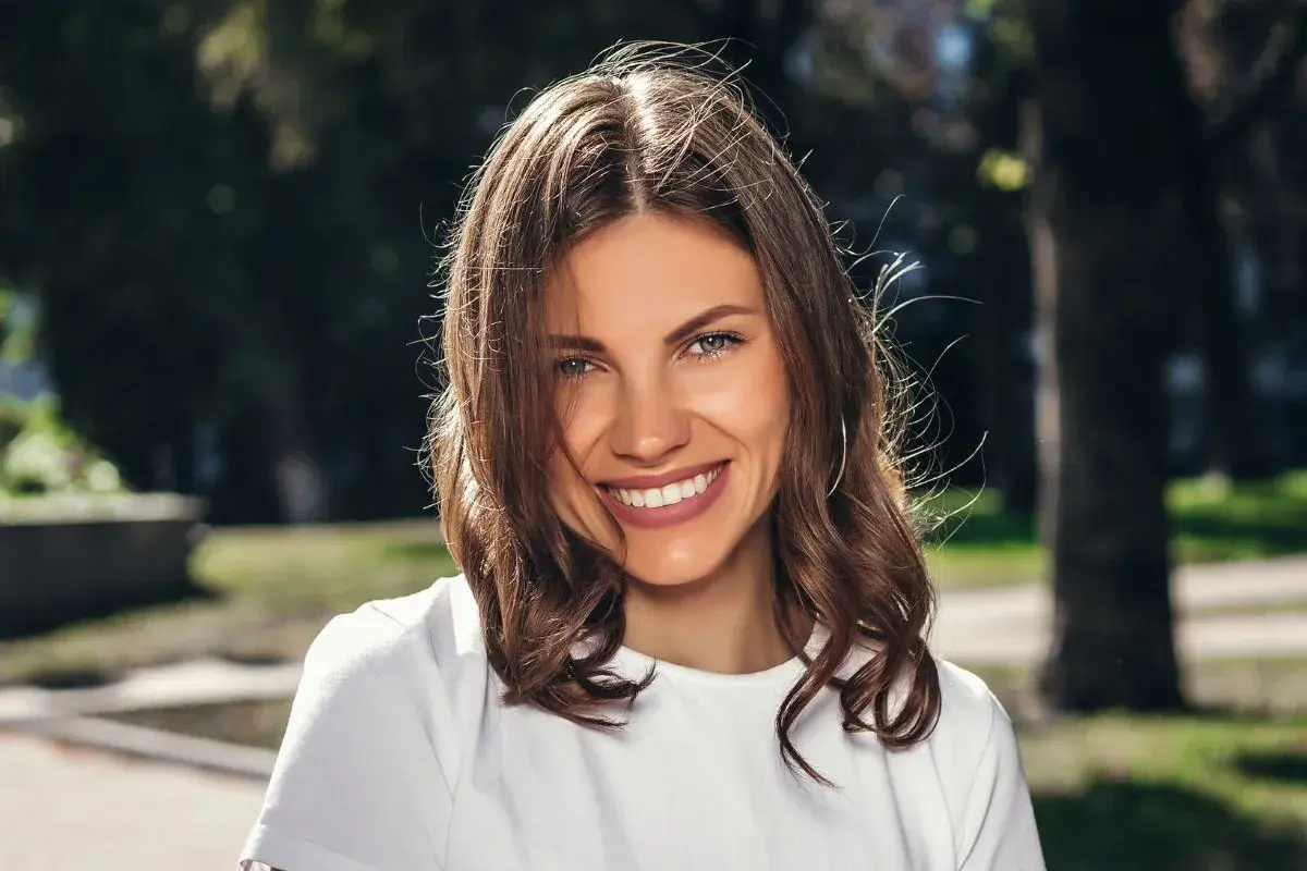 Uśmiechnięta brunetka w białej koszulce, idealna do zadawania pytań do nowo poznanej osoby.