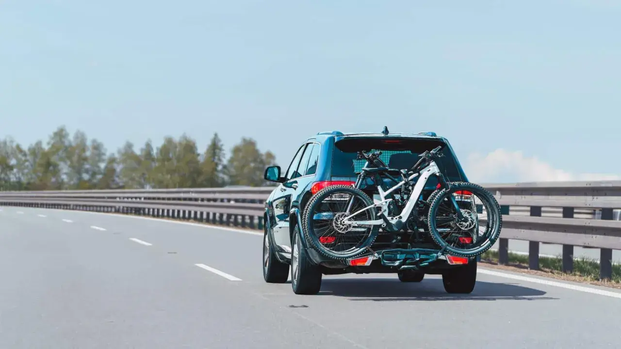 Un turismo transporta una bicicleta de montaña en un portabicicletas trasero. La carga sobresale considerablemente, pero es una forma común de llevar equipo deportivo.