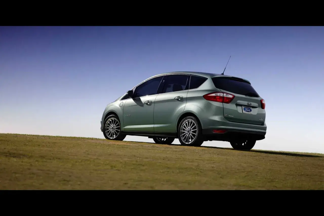 Ein hellgrüner Ford C-Max Energi Plug-in Hybrid steht auf einem grasbewachsenen Hügel unter blauem Himmel.