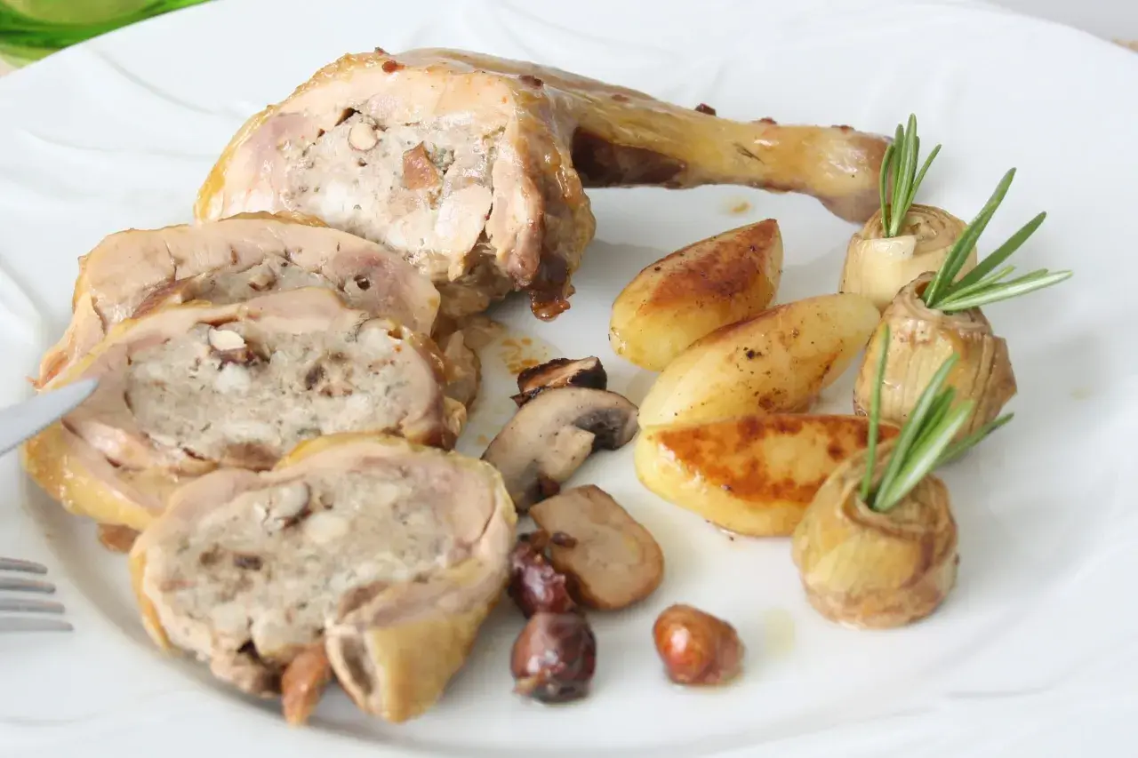Délicieuse cuisse de pintade farcie, servie avec des pommes de terre rôties, des champignons et des cœurs d'artichauts garnis de romarin.