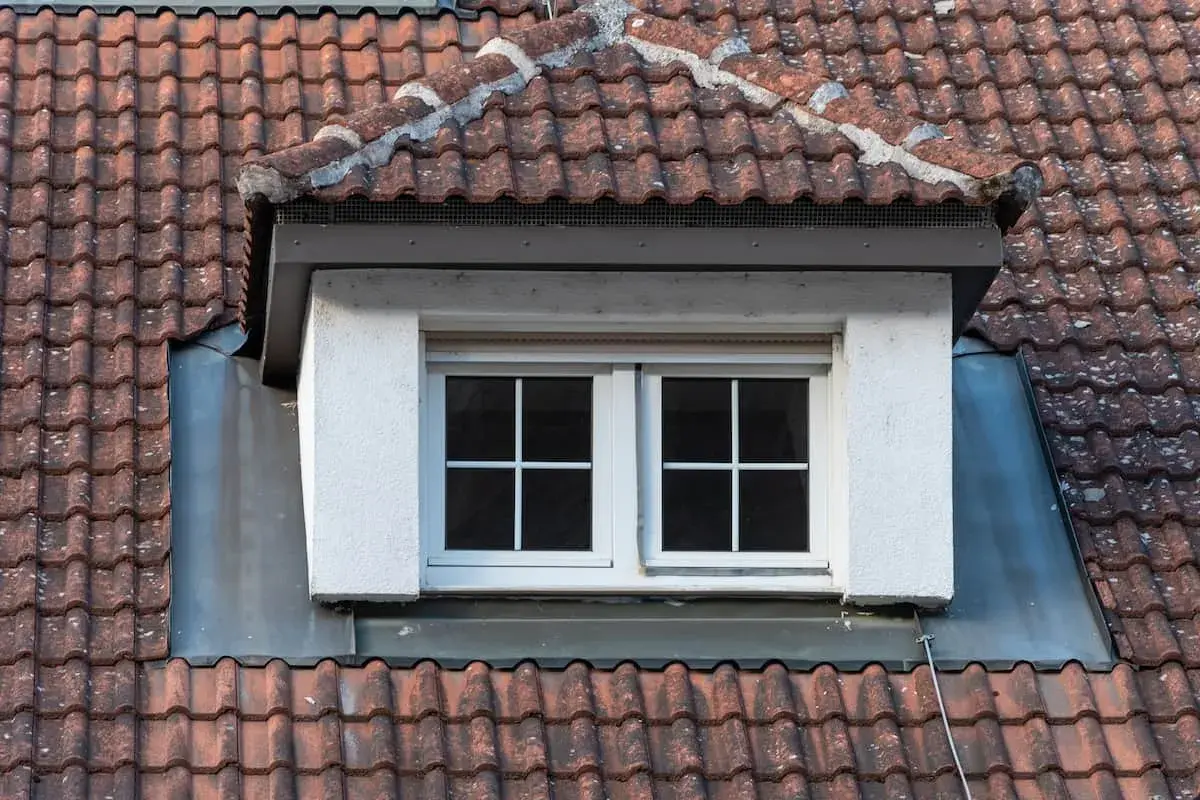 Dachgaube mit zwei Fenstern, umgeben von roten Dachziegeln. Die Bleiverkleidung zeigt, wie man eine dachgaube richtig abdichten kann.