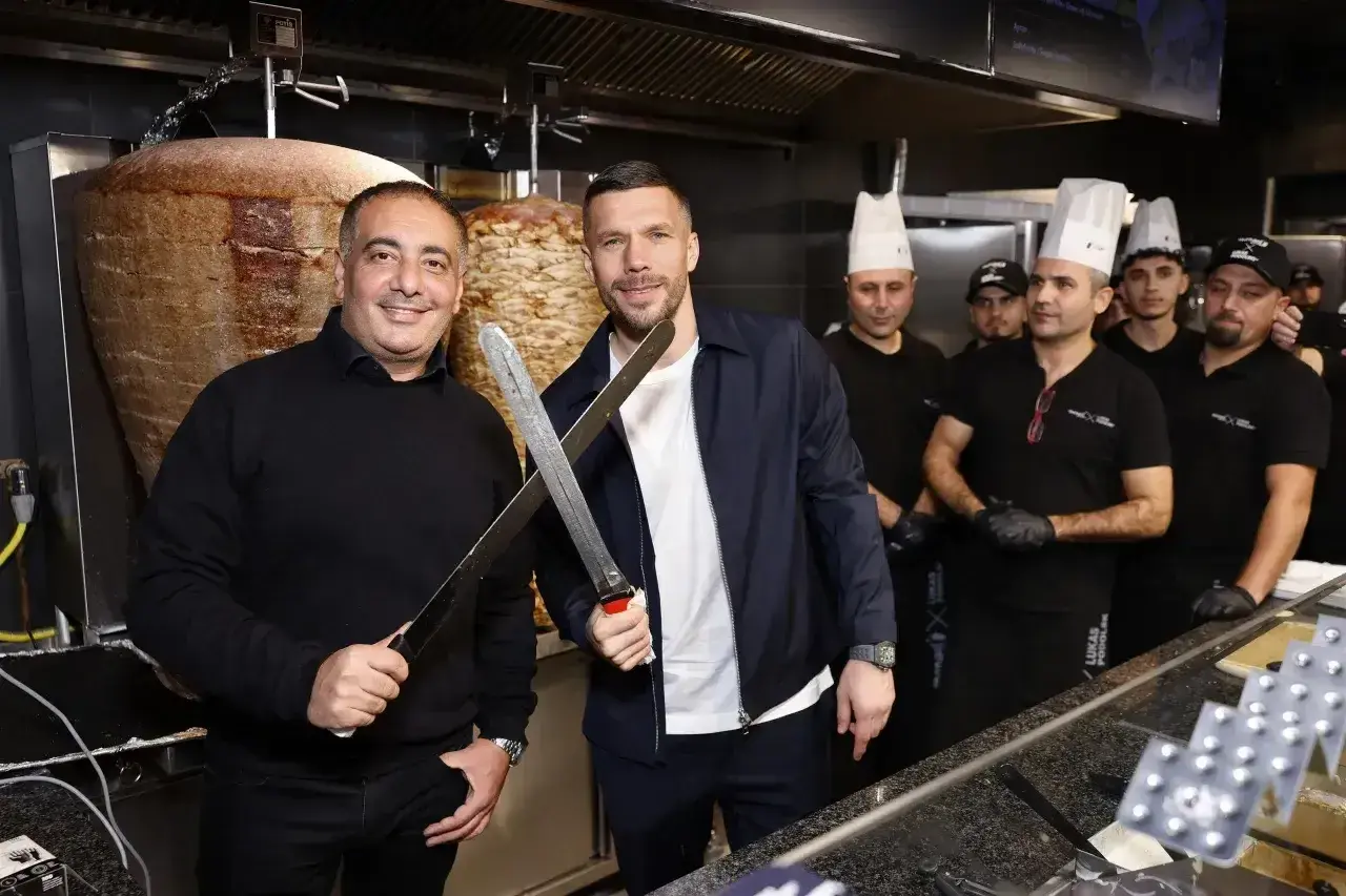 Lukas Podolski z nożami w ręku, obok niego pracownicy restauracji z kebabem.