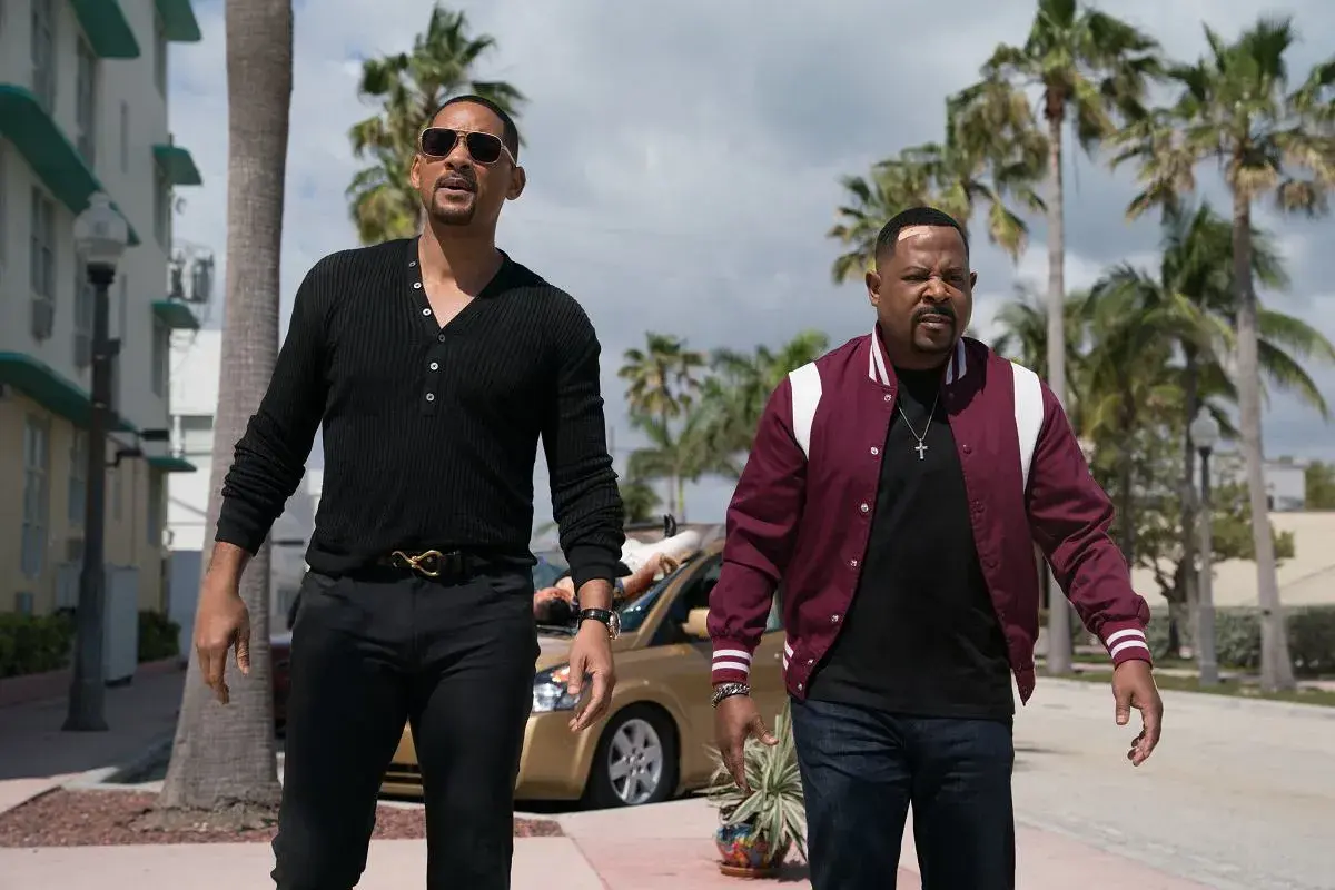 Will Smith i Martin Lawrence w filmach "Bad Boys" idą ulicą w słoneczny dzień, otoczeni palmami.