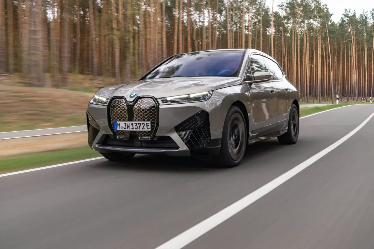 Szary BMW iX jedzie po drodze wśród drzew.