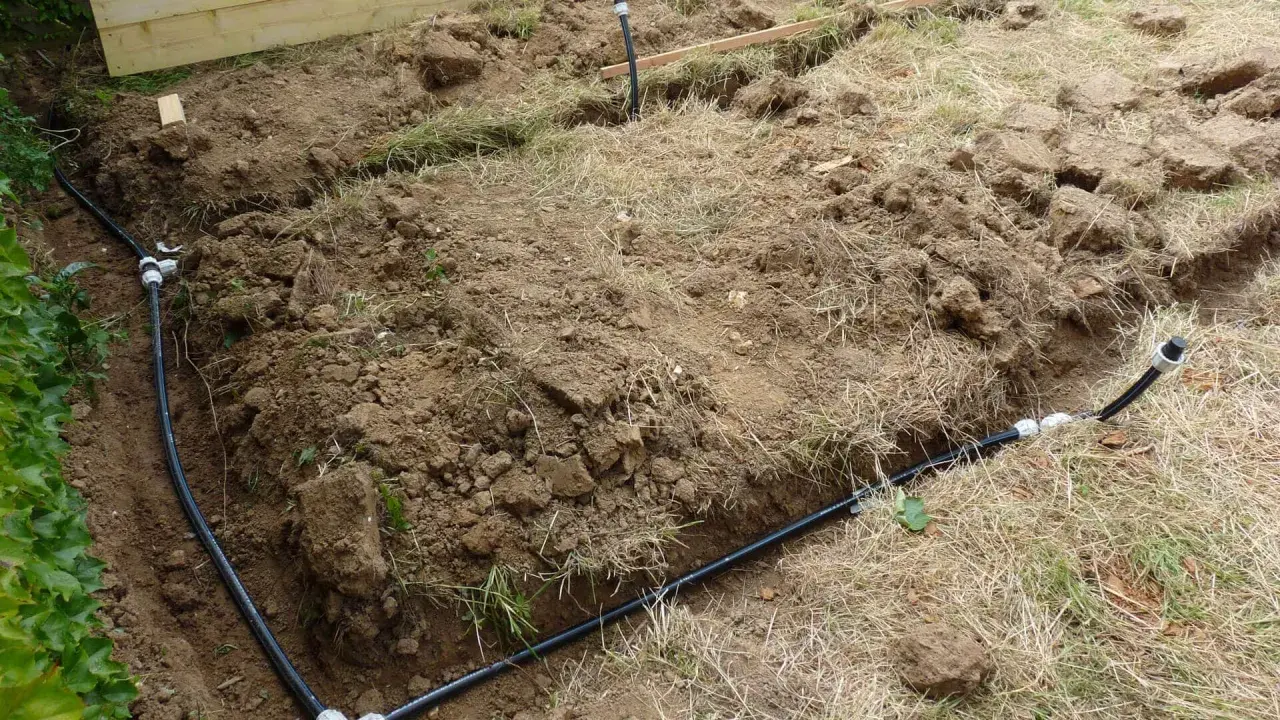 Des tranchées creusées révèlent des tuyaux noirs, prémices de réseaux enterrés pour l'irrigation ou le drainage.