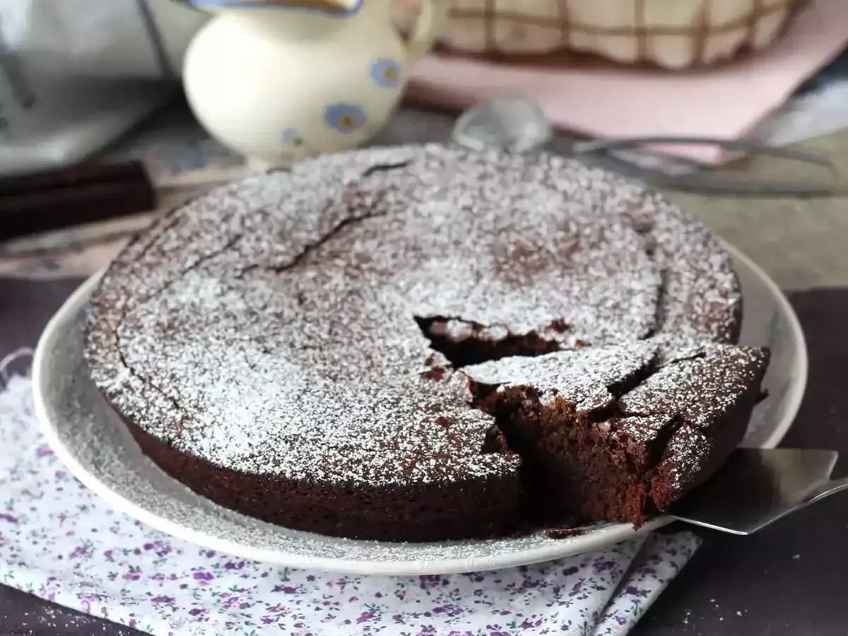 Un délicieux gâteau au chocolat saupoudré de sucre glace, parfait pour une recette gâteau au chocolat facile. Une part est coupée.