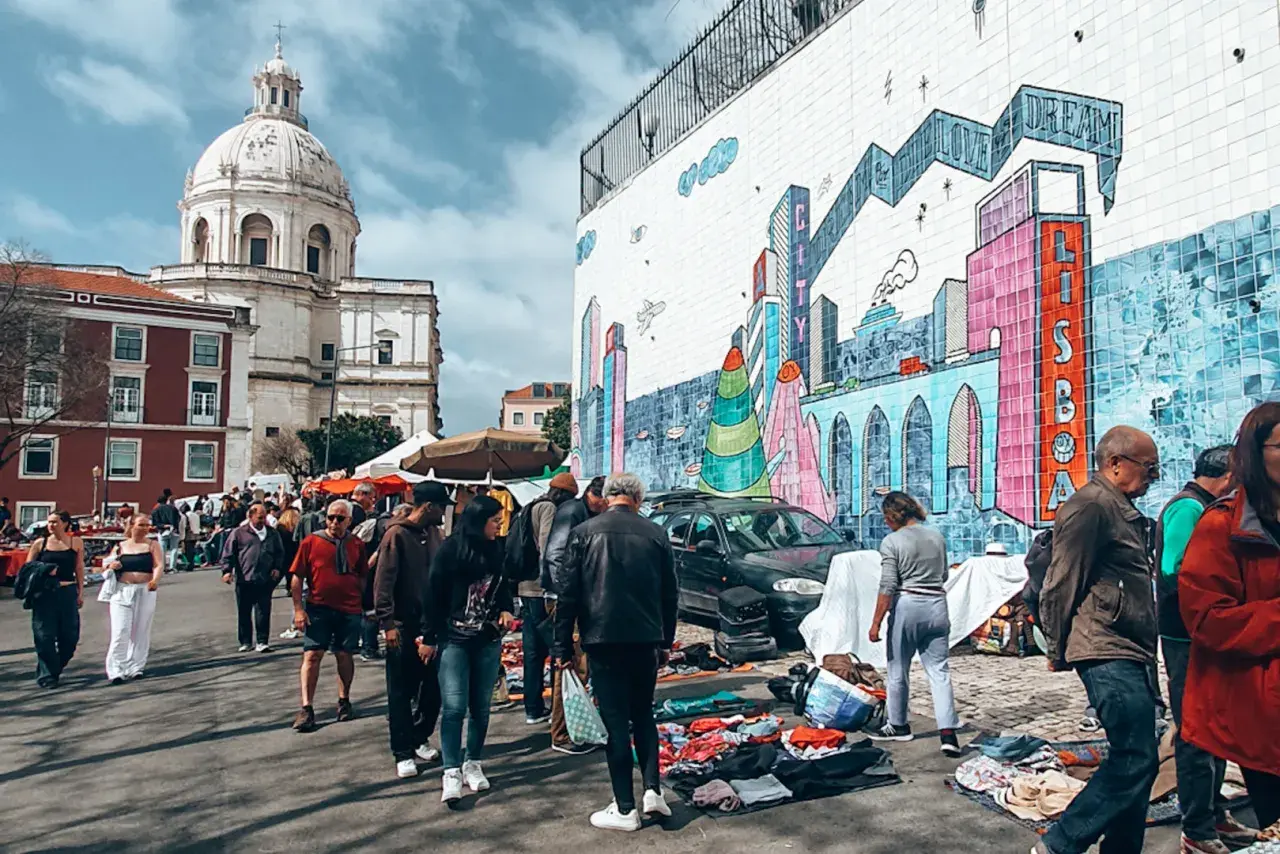 Bunter Flohmarkt in Lissabon mit Menschen, Kuppelkirche und Graffiti-Wand. Hier finden Sie echte Lissabon Geheimtipps.