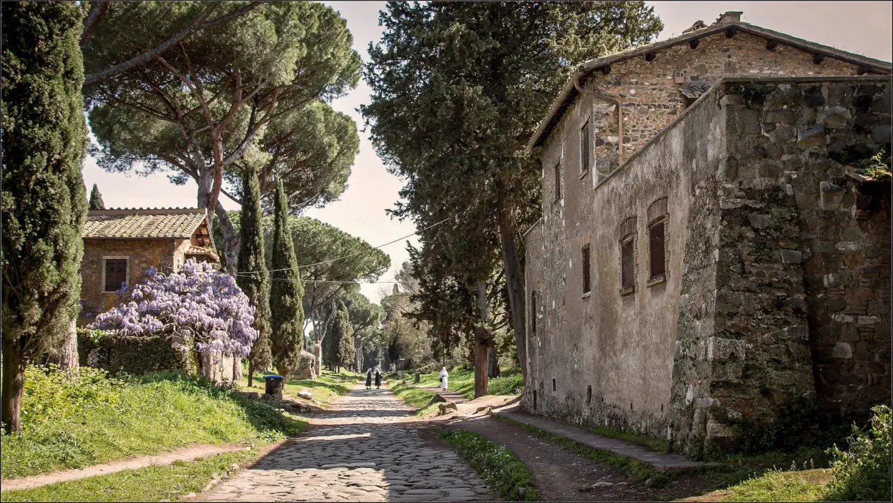 Une ancienne voie romaine à Rome, bordée de cyprès et de pins parasols, avec des maisons en pierre et des glycines en fleurs.