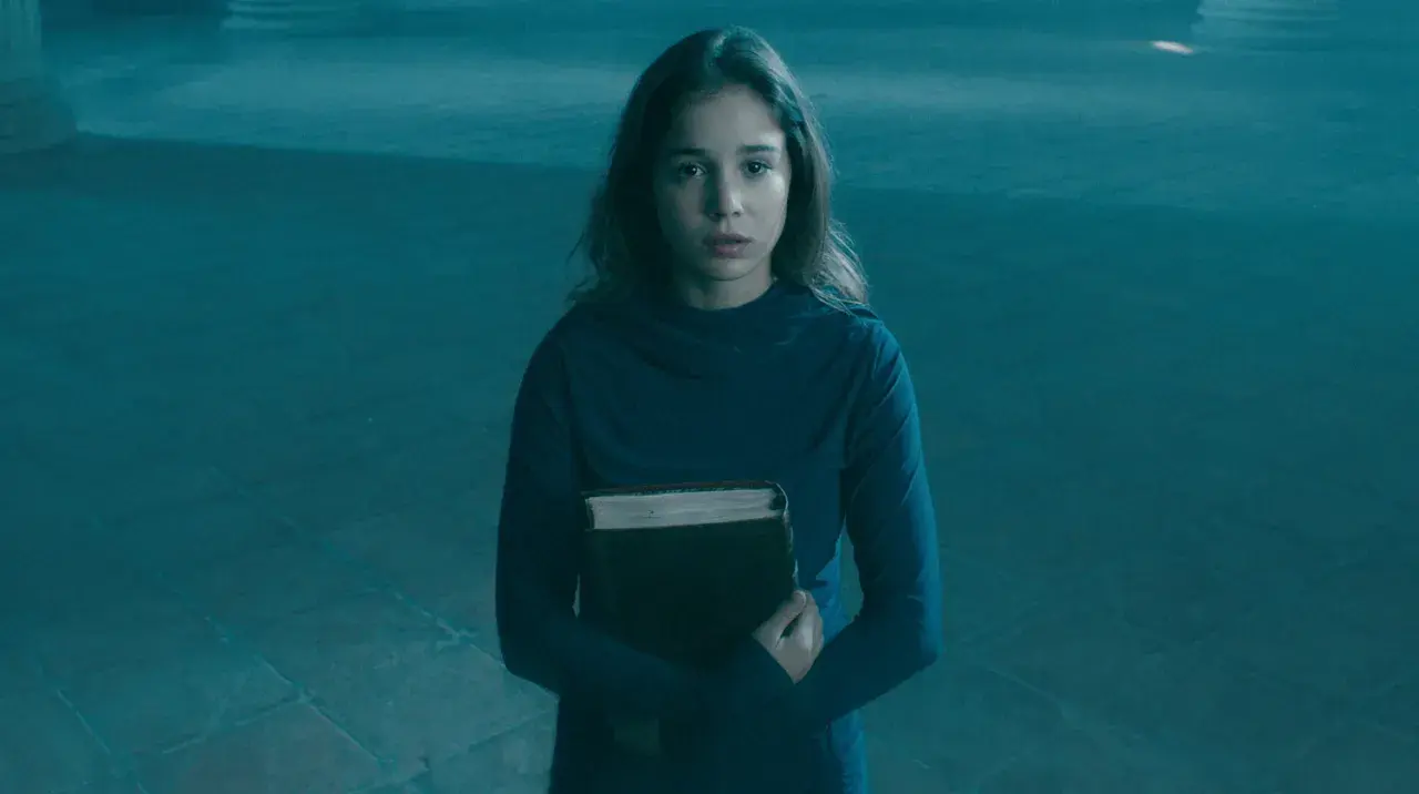 Alba Baptista, med en gammal bok i famnen, ser fundersam ut i det blåa ljuset.