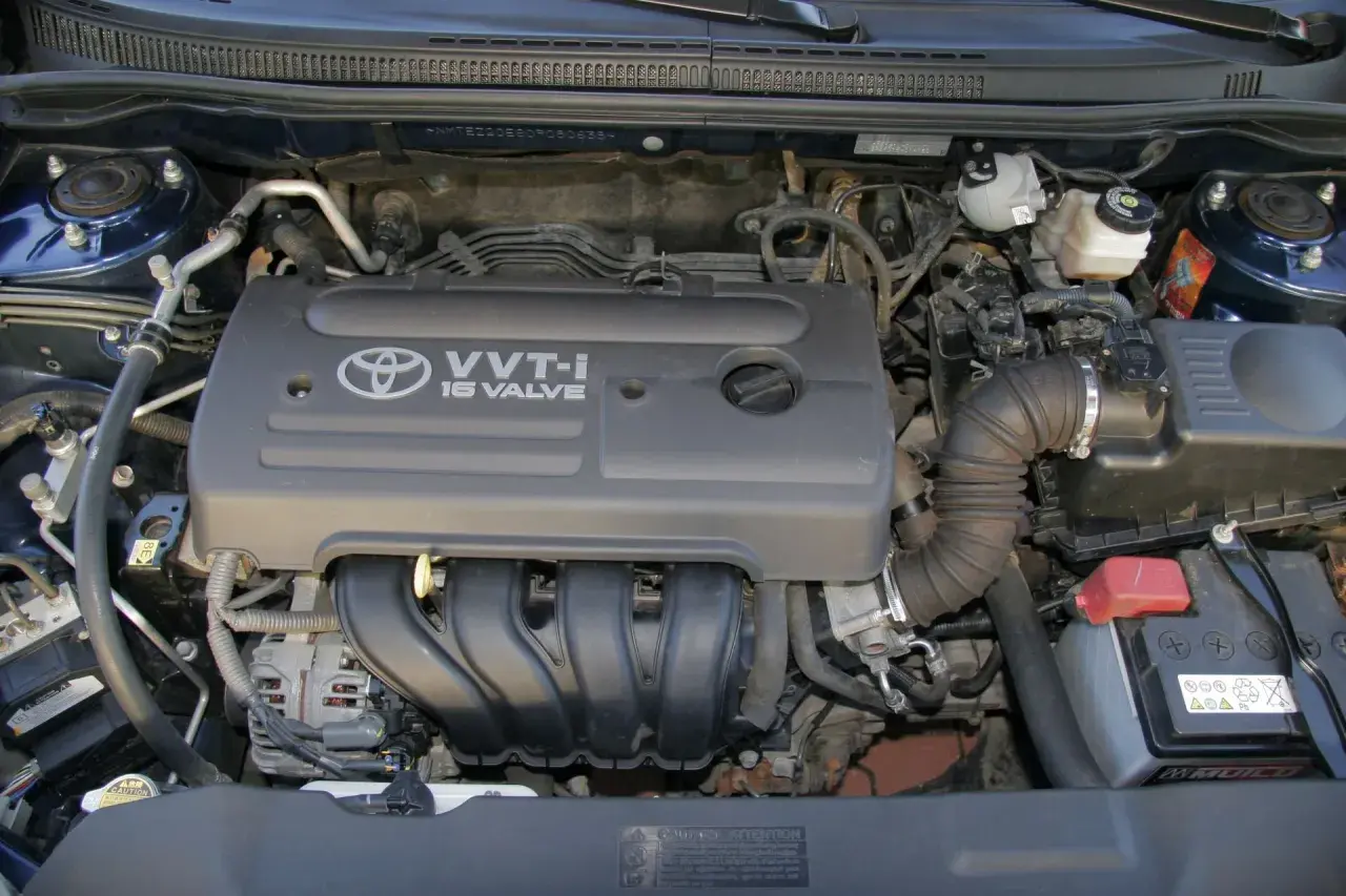 Silnik VVT-i 16 Valve z Toyoty Corolla E12. Widoczny alternator, akumulator i elementy układu dolotowego.