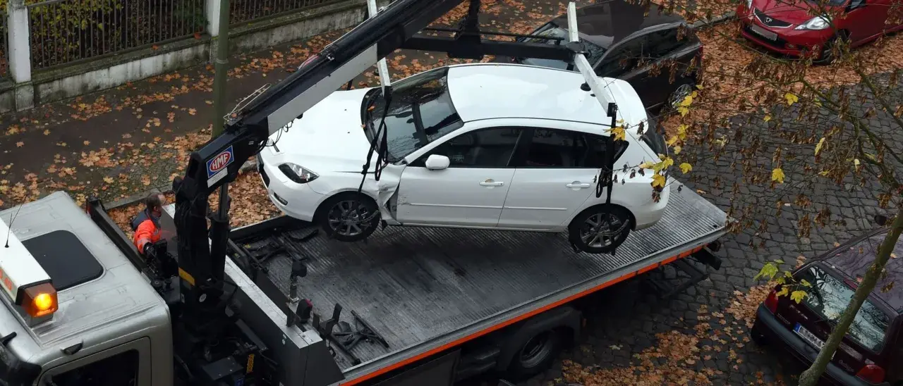 Ein Abschleppdienst hat ein weißes Auto auf einen LKW geladen. Das Auto wurde vorher weggefahren, da es beschädigt war.