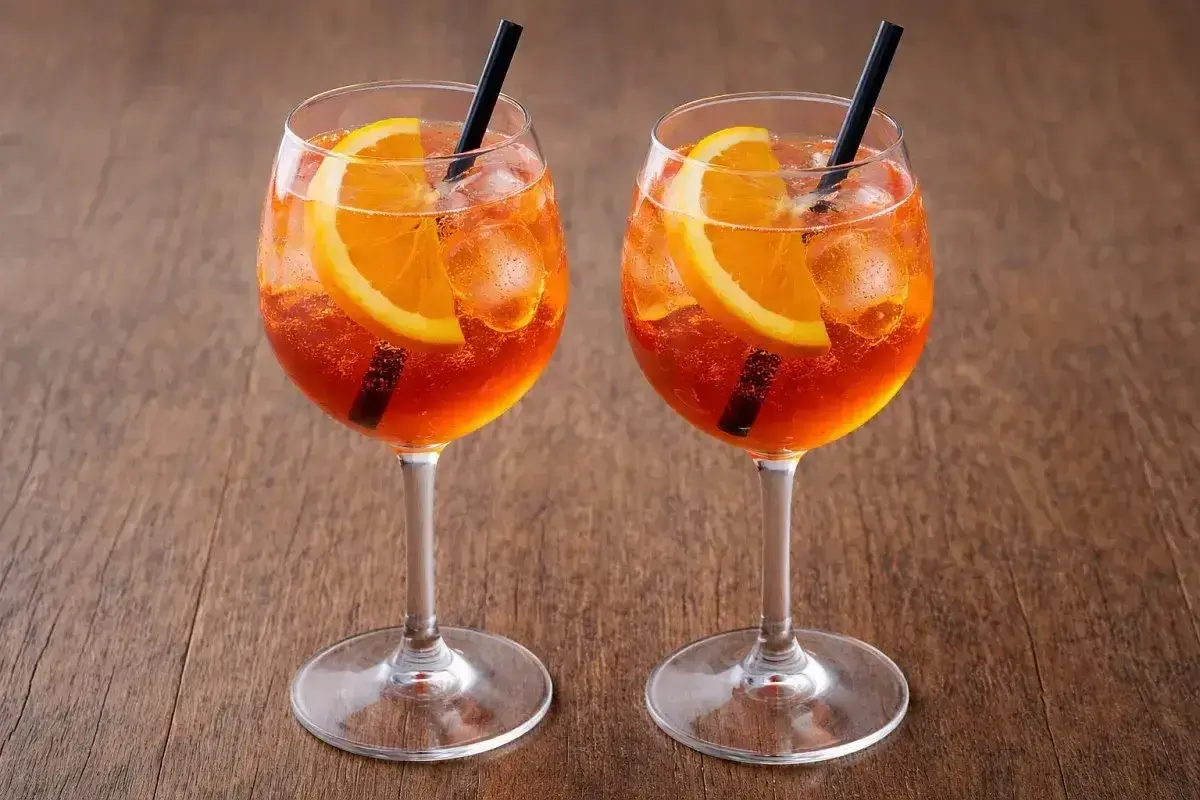 Dwa Aperol Spritz z pomarańczą i lodem, idealne aperol proporcje na drewnianym tle.