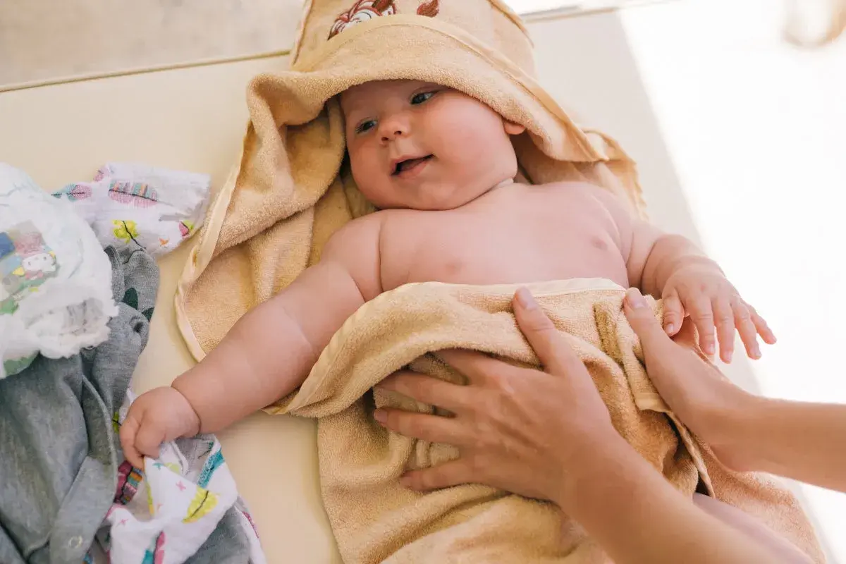 Söt bebis i handduk, kanske med tyst reflux bebis symtom. Bredvid ligger kläder och blöjor.