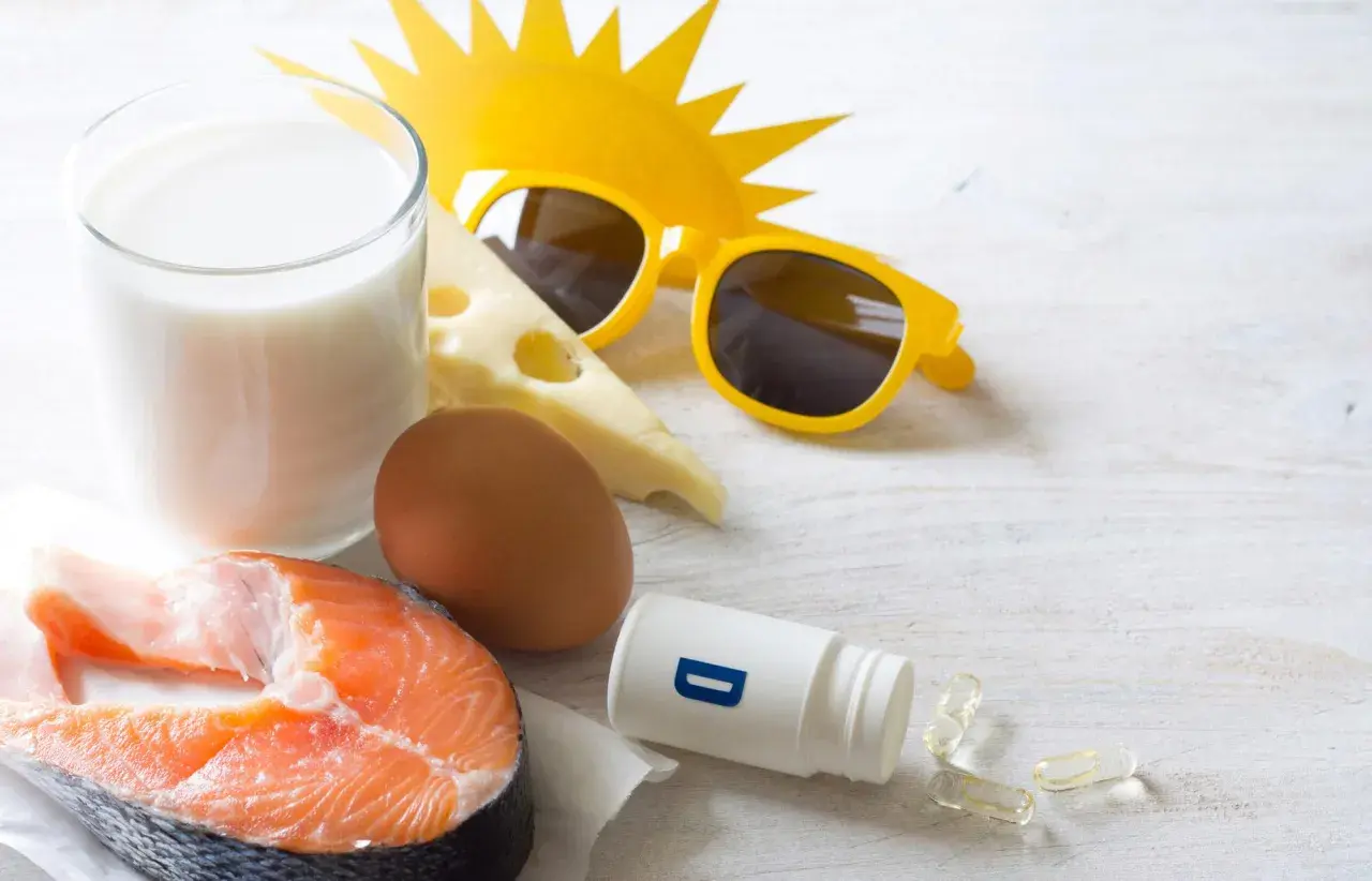 Zomerse zon, zonnebril en voedingsmiddelen die een stootkuur vitamine D bieden: zalm, ei, melk en kaas. Ook supplementen zijn zichtbaar.