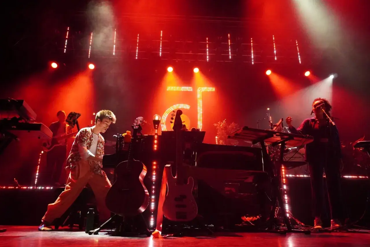 Jacob Collier and his band perform on a stage bathed in red light, with instruments and a large "GT" logo visible.