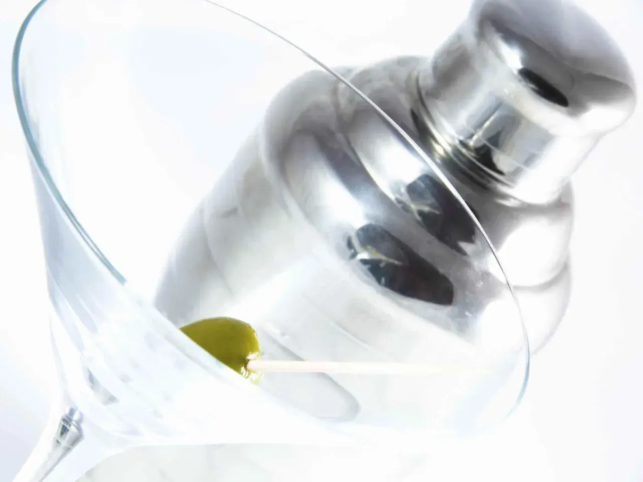 Verre à martini avec une olive, prêt pour une recette de martini gin. Shaker à cocktail en arrière-plan.