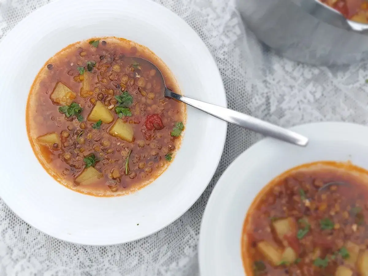 Herzhafte italienische Linsensuppe mit Kartoffeln und Kräutern in weißen Schalen, bereit zum Genießen.