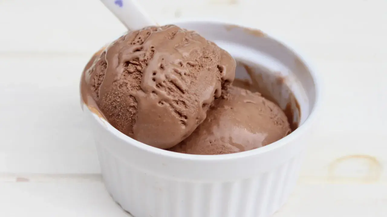 Dos bolas de cremoso helado de chocolate casero en un cuenco blanco, con una cuchara lista para disfrutar.